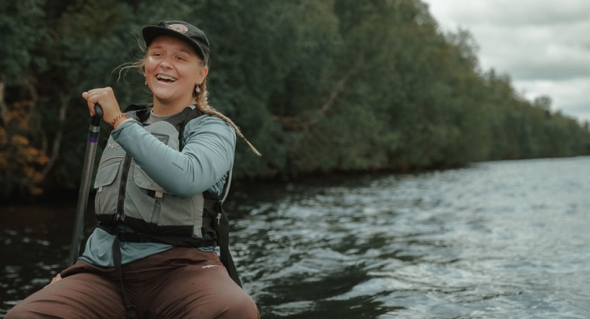 A person wearing a lifejacket and holding a paddle is sitting in a canoe and smiles for the photo.